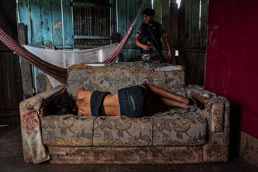 A woman lies on a sofa as a police officer searches for drugs in a shack used by crack cocaine users on Olarias street, in one of the most violent neighbourhoods in Altamira.