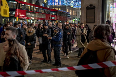 A policeman and a community support officer stand among the crowds of people out Christmas shopping on Oxford Street.