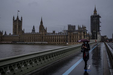A woman walks over Westminster Bridge, with the Houses of Parliament behind her, in the rain on the first day of Tier 3 restrictions in the capital.