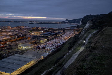 As trucks line up to board France bound ferries at the port of Dover a man cycles along the cliffs above.