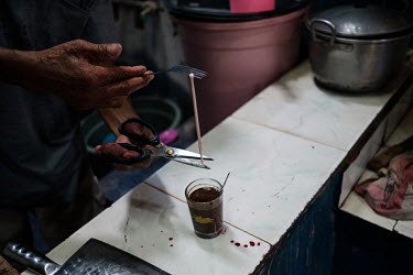 Samijan, a traditional healer, adding small pieces of the spinal cord from a spitting cobra to a potion for a customer in the kitchen at his family's home in Kediri. Samijan specialises in herbal poti...