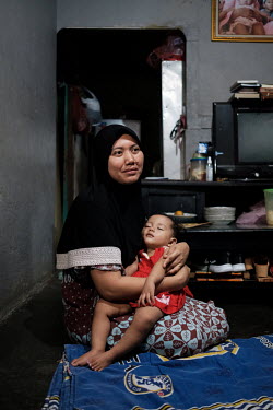Siti Raudoh with the youngest of her three children at her home in Tangerang. Her husband, Iskandar, a security guard, died from snake a bite after his finger was grazed by the fang of a snake that he...