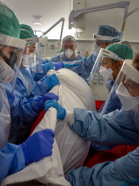 A team of seven people turn a patient with precise, safe motions onto their stomach so they are lying face down on T7, a temporary intensive care ward at University College Hospital. The prone positio...
