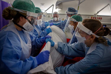 A team of seven people turn a patient with precise, safe motions onto their stomach so they are lying face down on T7, a temporary intensive care ward at University College Hospital. The prone positio...