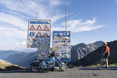 A bicyclist and a motorcycle parked beside a Italian-French border sign at Col Agnel in Le Queyras National Park in the French Alps.