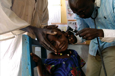 A father holds his daughter's head still while a medical worker checks inside her ears in the health centre at the Koubigou camp for internally displaced persons.