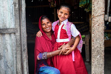 A girl, wearing school uniform, with her mother. The child has been able to stop labouring and start to attend school.