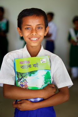 A student wearing his new uniform, and proudly clutching his text books, on his first day at school after he was able to stop labouring work and attend school for the first time.