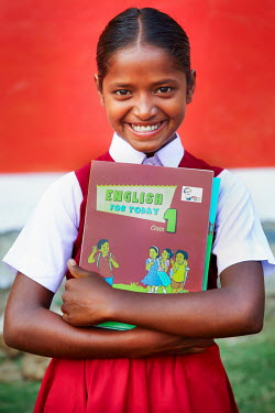 A student wearing her new uniform, and proudly clutching her text books, on her first day at school after she was able to stop labouring work and attend school for the first time.