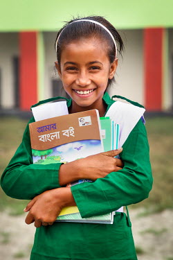 A student wearing her new uniform, and proudly clutching her text books, on her first day at school after she was able to stop labouring work and attend school for the first time.