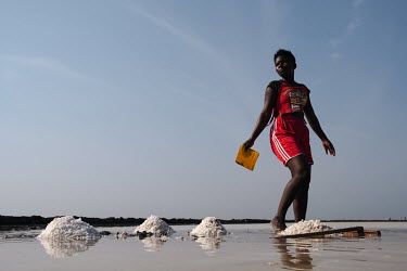 Helina Korley (20) working in a salt pan in the 'Yomo', the area traditionally held to be the spiritual heart of the salt-rich Songor Lagoon. A fashion design student at a nearby college, in her spare...