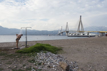 A man takes a fresh water shower after swimming in the sea near the Rio - Antirrio Bridge, the world's longest multi-span cable-stayed bridge which crosses the Gulf of Corinth near Patras.