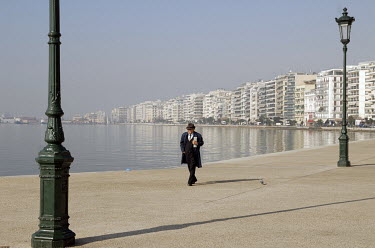 An elderly man walks along the Aegean seafront.