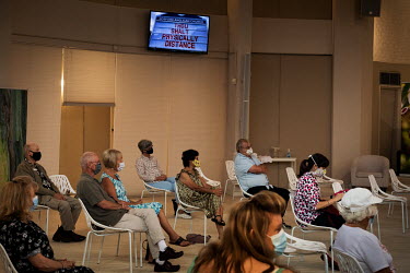 Churchgoers sit in social distanced formation as they wait for the beginning of a Sunday church service. A television shows an image of a recent billboard by Rod Bower with the words 'Thou shalt physi...