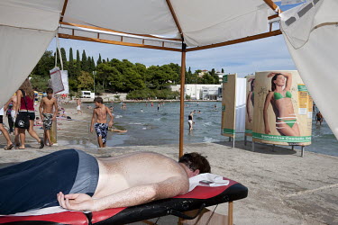 SA man lies on a bench in a massage tent on Bacvice city beach.