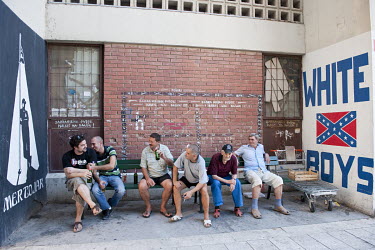 Locals are drink beer in the shadow of their block of flats on the outskirts of the city beside a mural of a Confederate flag with the slogan 'White Boys'.