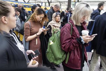 Passengers check their mobile phones while waiting on the platform at Rotterdam Central Station.
