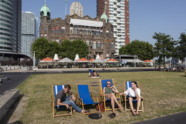 People relax on deck chairs in a small park in Kop van Zuid in front of the Hotel New York.