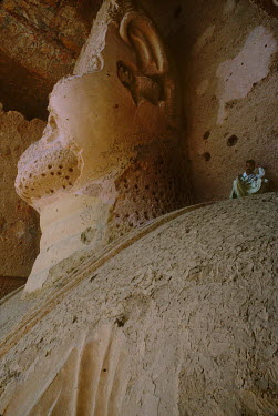 A man sits beside the head of the 'Eastern' Bamiyan Buddha (6th century CE), one of two giant rock-carved Buddha statues, prior to their destruction by the Taliban in 2001.