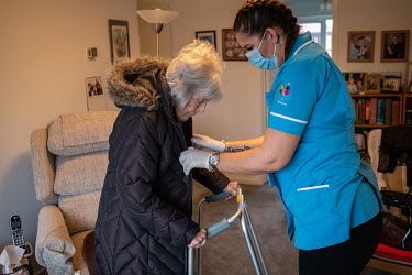 A care assistant helps a 90 year-old woman get ready to visit a vaccination centre for her second Pfizer-BioNTech vaccination to protect her against COVID-19.