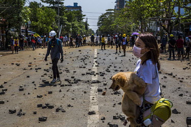 A woman carries her dog as she walks past the frontline where anti-coup protestors have gathered in Tharketa township to wait for the security forces crack down.
