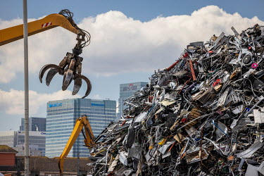 A scrap metal yard in the Lea Valley with high rise towers in Canary Wharf containing the headquarters of Barclays and Citigroup rising behind. The huge mound of ferrous scrap was growing because the...