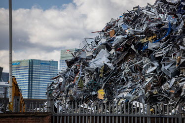A scrap metal yard in the Lea Valley with high rise towers in Canary Wharf containing the headquarters of Barclays and Citigroup rising behind. The huge mound of ferrous scrap was growing because the...