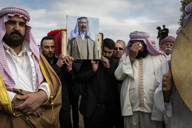 A photograph of a Yazidi man displayed on one of the coffins being carried by pallbearers during a funeral procession for 103 Yazidis murdered by ISIS in the village of Kocho in 2014. Having been exhu...