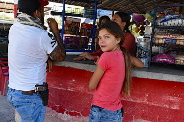 A member of 'Los Viagras', an armed vigilante group that call themselves 'grupos de autodefensas' (self-defence militias), talking to a woman working in a stall while on patrol. The controversial vigi...