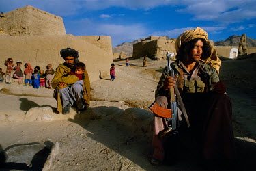 A mujahedin fighter sits near village children.
