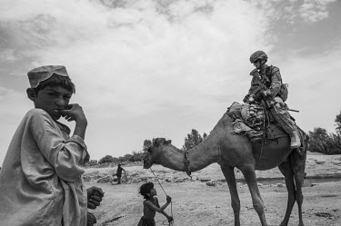 A US marine sits on a camel led by a child as he participates in a security patrol.