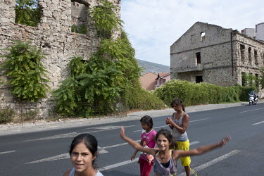 A group of Roma gypsy children walk along a road that passes a row of bombed out houses on the former front line of the war between Muslim Bosniaks and Croats.