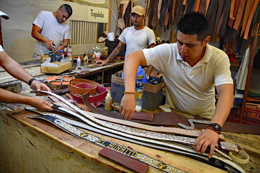 Inmates making leather belts in a prison workshop where prisoners make artisanal products for sale.