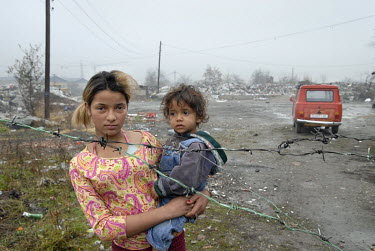 A Roma gypsy woman with a child in her arms stands behind barbed wire fencing in the waste dump where her family lives near the city's train station.