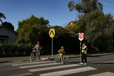 A mum and her child walk over a road at a zebra crossing with the help of a 'lolly pop' traffic controller on their way home from school, on a busy road in Mullumbimby in the Byron Bay shire.  The Byr...