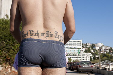 A man walking beside the Adriatic Sea coast with a tattoo on his back that reads: 'Get rich or die tryin'.