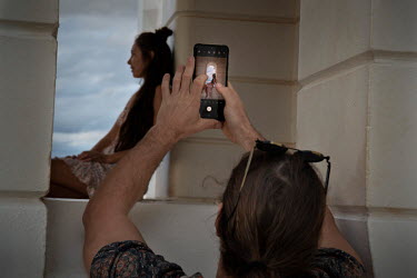 The partner of a young woman takes photographs of her at the Byron Bay Lighthouse, a popular location for tourists.   The Byron Bay community is at war with a proposed Netflix reality TV show called B...