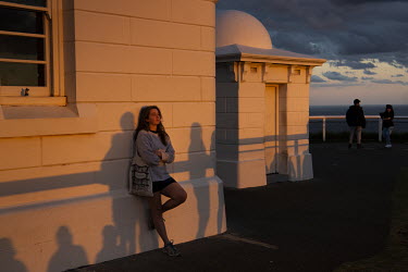 Sophie Jackson watches the sunset from behind the crowd at the base of the Byron Bay Lighthouse.   The Byron Bay community is at war with a proposed Netflix reality TV show called Byron Baes, which lo...