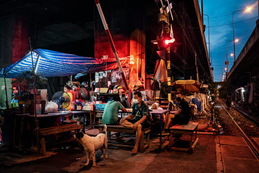 Residents of the Klong Toei slum community gather in the evening outside homes along a railway track and under a highway.