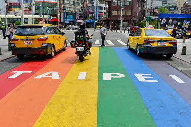 An Uber Eats delivery motorbike and two yellow taxis on a pedestrian crossing painted in rainbow colours in the Ximending youth entertainment and fashion area of downtown Taipei.
