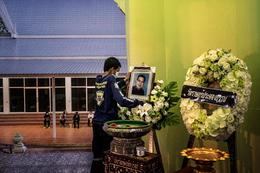 A rescue worker places the portrait of a 68 year old factory owner, who died of COVID-19, in a temple where he will be cremated as family members stay seated outside for social distancing purposes.