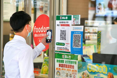 A man using a track and trace QR Code App on his mobile smart phone before entering a convenience store in central Taipei.