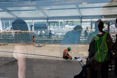 Geneva Summit Preparations at the lakeside Media Centre. Member of the press stand inside while sunbathers by the lake are refelcted in the window. On 16 June 2021 US president Joe Biden and Russian p...