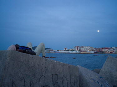 As a full moon rises, a West African migrant rests on concrete sea defences near the port where many migrants are camped trying to evade police after illegally entering the Spanish exclave of Ceuta wh...