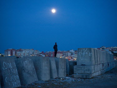 As a full moon rises, a West African migrant stands on concrete sea defences near the port where many migrants are camped out trying to evade police after illegally entering the Spanish exclave of Ceu...