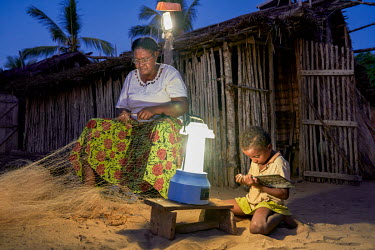 'Solar Mama' Yollande Randrianambinina repairs a fishing net using the light from a solar lamp while her grand-daughter studies beside her.   Dubbed the 'Solar Mamas', these women were the first in th...