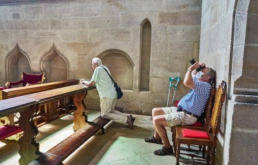 A man praying while another man photographs new restoration work in the Cathedral of St. Bartholomew.
