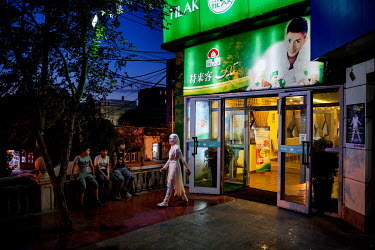 Youths sitting outside a restaurant endorsed by Uighur pop sensation Ablajan, who's picture is on the hording above the entrance.