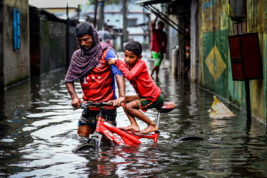 A man pushes his son, on a bicycle, along a street thigh deep in flood water.  Water is essential for survival, yet in Bangladesh water also has the power to destroy anything in its path. For months a...