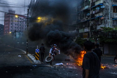A flashmob of young protestors burn tires and leave bricks and rubbish on the main road while security forces clear other roadblocks and patrol inside their neighbourhood, in Tamwe township.